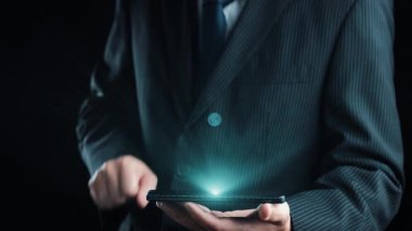 Bir işadamı, sürdürülebilir enerji ve yeniliği sembolize eden rüzgar türbini ve pil ikonları da dahil olmak üzere ekoloji temalı grafikleri gösteren etkileşimli bir tablet sunuyor. Dörtgen