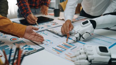 Modern bir çalışma alanında, insan ve robot eller veri grafiklerini analiz etmek, teknoloji ve takım çalışmasının karışımını bir iş toplantısında göstermek için işbirliği yaparlar. Noogenesis