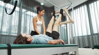 Cadillac ekipmanları üzerinde bacak kaldırma egzersizinde müşteriye yardımcı olan yetenekli pilates eğitmeni. Kadın antrenör, Cadillac 'ın bacak gerdirme hareketine yardım ediyor. Temel bağlantıyı geliştirmek için, bacak esnekliği için. Alışkanlık.