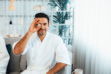 Elinde taze salatalık dilimleri tutan ve bornoz giyen bir adam tatil köyünde ya da otelde yüz bakımının keyfini çıkarıyor. Yüz ve güzellik tedavisi için cilt bakımı. Sessiz.