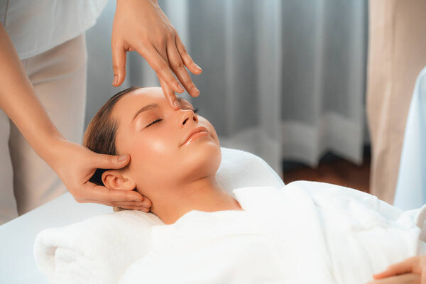 Caucasian woman enjoying relaxing anti-stress head massage and pampering facial beauty skin recreation leisure in dayspa modern light ambient at luxury resort or hotel spa salon. Quiescent