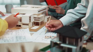 Bir grup profesyonel, modern bir ofis alanında mimari modeller ve teknik planlar üzerinde işbirliği yaparak takım çalışması ve tasarımda yaratıcı çözümler sergiliyor. SACTR