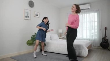 Yatak odasında Asyalı kızıyla müzik eşliğinde dans eden mutlu çekici anne. Beyaz anne dans eder ya da egzersiz yapar. Bu arada tatlı çocuk da müzik eşliğinde yatağa atlar. Aile eğlence konsepti. Pedagoji.