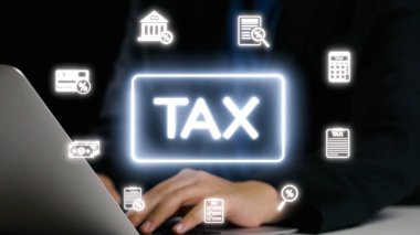 Vergilerle ilgili çeşitli simgelerle çevrili bir dizüstü bilgisayar kullanan, modern mali yönetimi, bütçeyi ve dijital kayıt tutmanın önemini temsil eden bir kişi. Dörtgen