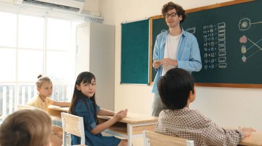 Matematik formülü veya teorisi ile karatahtanın önünde dururken sınıfın etrafına bakan profesyonel akıl hocası. Çeşitli ilköğretim öğrencileri matematik dersinde öğreniyor, çalışıyor ve oturuyor. Pedagoji.