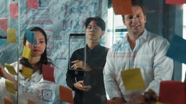 Cam duvarda yaratıcı fikirleri paylaşmak için renkli yapışkan notlar kullanarak pazarlama fikrini değerlendiren mutlu profesyonel iş adamları. Bir grup farklı iş adamları strateji hakkında tartışıyorlar. Yönlendirici.