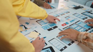 Modern bir ofiste dinamik bir sahne gösterisi ekibi işbirliği. Bireyler, dijital cihazları ve notları masaya yayılmış olan kullanıcı arayüzü tasarımları üzerinde beyin fırtınası yapmakla meşguldürler. SACTR