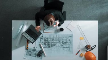 Dizüstü bilgisayarda çalışırken mimari çizimlerin hava görüntüsü. Kafkasyalı mühendisin bina modelini tasarlayıp, ekipman ve güvenlik kaskıyla birlikte tasarladığına dair tepeden aşağı bir bakış açısı. Hizalama.