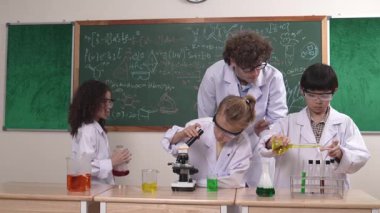 Kafkasyalı zeki öğretmen, meraklı öğrencilerin laboratuardaki deney kabına renkli sıvı dökmesini destekler. Yaratıcı çocuklar deney yapmaya ve biyokimyasal örnekleri incelemeye konsantre olurlar. Pedagoji.
