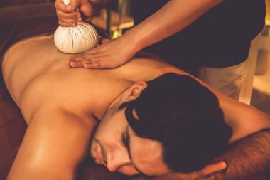Sıcak bitkisel top spa masaj vücut tedavisi, masör erkek vücuduna nazikçe şifalı bitki torbası bastırıyor. Aromaterapi tesisinin sakinliği ve dinginliği kaplıca salonundaki mumların sıcacık ışığında. Sessiz.