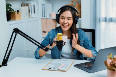 Sosyal medyada kulaklıkla canlı yayın yapan Asyalı sunucu modern stüdyoda yaşam koçluğu veya pazarlama dinleyicilerini selamlıyor. Taktik.