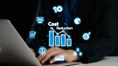 Bir işadamı, gelişmiş finansal grafikler ve profesyonel bir ortamda bir dizüstü bilgisayardaki etkileşimli veri görselleştirmeleri kullanarak maliyet azaltma stratejilerini değerlendirir. Dörtgen