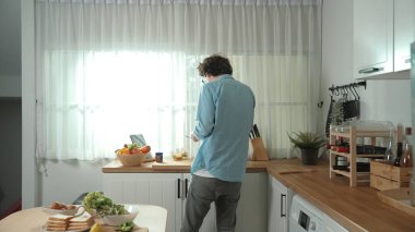 Mutlu baba yemek pişirirken müziğe geçiyor ve modern mutfakta öğle yemeği hazırlıyor. Aktif baba, sebze ve mutfak gereçleri ile çevrili sağlıklı yemek ya da salata yaparken şarkıyla dans ediyor. Pedagoji.