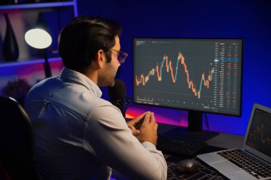 Akıllı tüccar işadamı, karanlık oda gecesinde neon ışıklı ofisteki arama pazarında yüksek kârla ekranda bilgisayar ve bilgisayar üzerinde dinamik borsa yatırımları üzerinde yoğunlaşıyor. Tahmin et..