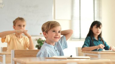 Sınıfta okuyan çeşitli çocuklarla çevrili beyaz bir çocuk öğretmenine soru sorup cevap verdiği için elini kaldırıyor. Mutlu öğrenci birlikte çalışıyor, oy veriyor, gönüllü oluyor, hocayı arıyor. Pedagoji.