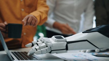 Profesyonel bir toplantı sırasında dizüstü bilgisayarla etkileşime giren bir robotun yakın plan görüntüsü, modern çalışma ortamlarında teknoloji ve insan işbirliğinin entegrasyonunu vurguluyor. Noogenesis