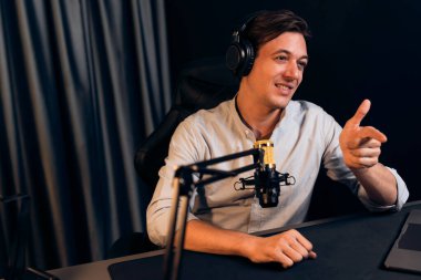 Sunucu kanalı akıllı yayıncı laptopta canlı sosyal medya uygulaması arıyor, kulaklık takıyor ve modern ofis stüdyosundaki mikrofonu kullanıyor. Bireysel.