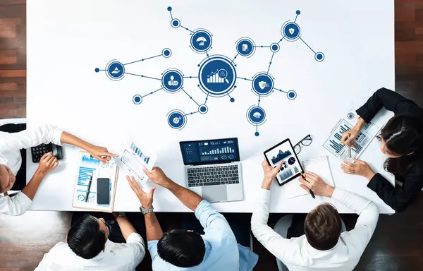 Çeşitli bir ekip, modern bir çalışma alanında iş yönetimi stratejileri ve veri içgörülerini tartışmak için dijital araç ve grafiklerden yararlanarak, işbirlikçi bir toplantıya katılıyor. Dostluk