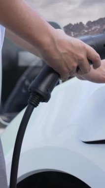 İlerici adam şarj noktasında elektrikli araba yüklüyor, daha temiz bir çevre için temiz ve yenilenebilir enerjiyle çalışan bir EV ile doğada ve dağlarda seyahat ediyor..