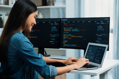 IT geliştiricisinde gülümseyen genç Asyalı dizüstü bilgisayarında kodlama programı verileriyle kotlu tişört giyerek çevrimiçi bilgi yazıyor. Güvenlik analizi iki ekran ile çevrili. Taktik.