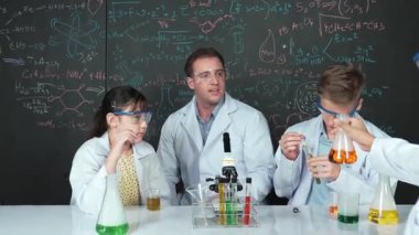 Zeki kız, çeşitli öğrenciler STEM fen dersinde deney yaparken renkli sıvıyı inceliyor. Bir grup liseli çocuk tahtada dururken laboratuvarda çalışıyor. Yaratıcı. Öğretim