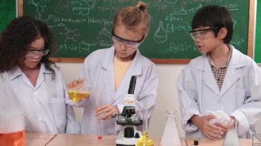 Kafkasyalı öğrenci deney yapıyor ve laboratuvarda yeni yenilikler keşfetmek için bekleyen meraklı çocuklarla çevrili biyokimyasal solüsyon döküyor. Çeşitli mutlu öğrenciler deney yapıyor. Pedagoji.