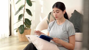 Kanepede oturan bir kadın ders kitabı okuyarak sosyal ve mesleki teknoloji bilgisini artırır ya da akıllı bir anne olmak için çocuk yetiştirir. Hayat boyu öğrenme konsepti. Uyumsuzluk.