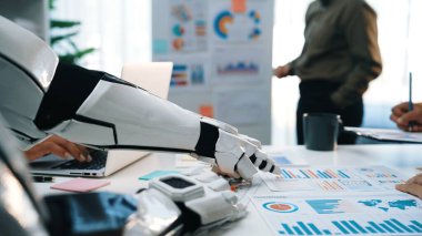 Bir robot kol, veri analizi ve raporlara odaklanan bir iş toplantısına yardımcı olur. Modern ofis takım çalışması ve teknolojisini işbirlikçi bir ortamda sergiliyor. Noogenesis