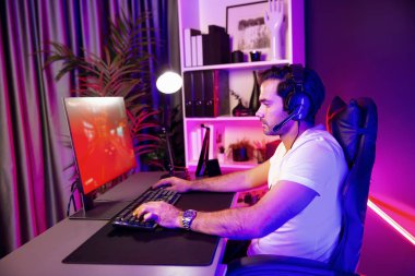 Kulaklık takan akıllı oyun flaması hafta sonu neon dijital siber ışıklandırma odasında son yaşam tarzı yarışmasında şampiyon olmak için bilgisayar ekranında araba yarışı oynamaktan zevk alır. Tahmin et..