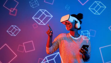 VR gözlüklü Afrikalı kız mavi ve pembe arka planda duruyor ve yüzen geometrik şekle bakıyor. Heyecanlı insan görsel gerçeklik dünyasına giriyor. Teknoloji yeniliği. Yaratıcılık.
