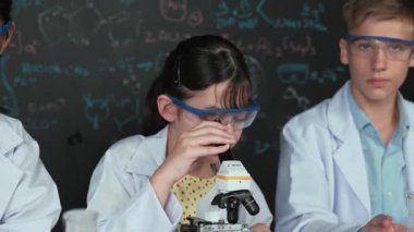 Öğrenci tahtada teoriyle deney yaparken güzel bir kız mikroskop altında araştırma yapıyor. Genç bilim adamı renkli çözeltiyi deneysel ekipmanlarla inceledi. Öğretim