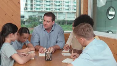 Çok kültürlü çocuklar resim çizerken ya da masa başında kalemle kağıt üzerinde not alırken zeki öğretmen konuşuyor ve işi anlatıyor. Otururken çeşitli öğrenci çizimleri ya da paylaşım fikirleriniz kutlu olsun. Öğretim