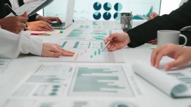 Modern ofis ortamında tablolar ve istatistiklerle çevrili bir toplantıda çeşitli iş adamları veri analizine girişiyor. SACTR