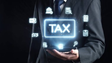 Bir işadamı, modern muhasebede dijital hizmetler ve mali yönetimin kesişimini temsil eden aydınlatılmış vergi simgelerinin yer aldığı bir tablet sergiliyor. Dörtgen