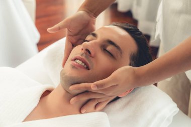 Beyaz adam stres önleyici kafa masajından ve lüks bir tatil beldesi veya otel spa salonundaki modern ışık ortamında yüz güzelliği eğlencelerini şımartmaktan hoşlanıyor. Sessiz.