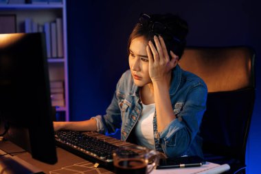 Stresli, genç, güzel Asyalı yaratıcı proje yaratıcısı sosyal medyayı araştırmak için bilgisayara bakıyor ve geceleri daha çok neon modern ofisin planlama kanalı stratejisine ulaşılıyor. Taktik.