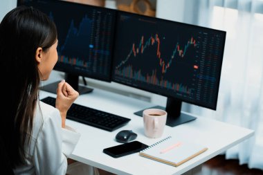 Başarılı genç Asyalı iş kadını, modern ofisteki bilgisayar ekranlarında dinamik iş grafiği üzerine borsada yumruklaşarak en yüksek karı elde ediyor, finansal teknolojiyi analiz ediyor. Taktik.