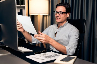 Akıllı iş adamı iş paragrafı dinamik veri tabanı pazarlama analizi planlama tablosuna bakıyor. Etrafı kağıt kağıtları ve bilgisayar monitörü raporlarıyla çevrili. Bireysel.