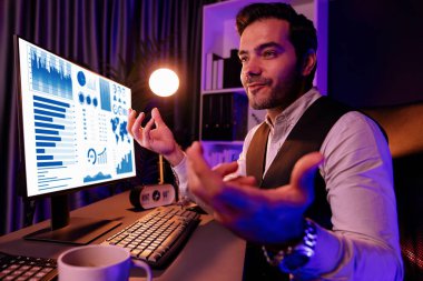 Gülümseyen zeki işadamı, uzaktan da olsa satış ekibiyle çevrimiçi olarak buluşuyor ve gece vakti Neon Dark Light Home Office 'deki bilgisayar ekranında ürün veritabanındaki araştırma hedef pazarını tartışıyor. Tahmin et..