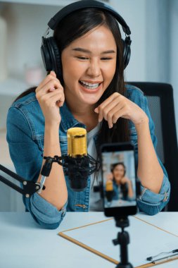 Asyalı sunucu canlı yayında canlı yayında canlı yayında sosyal medyada kulaklık takarak konuşuyor. Dinleyicileri modern stüdyoda koçluk yaparak selamlıyor. Taktik.