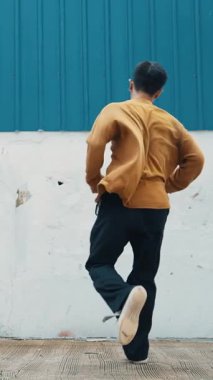İspanyol adam kollarını açıp duvarın önünde dans ediyor. Dansçı ya da koreografın günlük kıyafetleriyle hip hop tarzında break dans yaparken ki görüntüsü. Açık hava sporu 2024 hiphop..