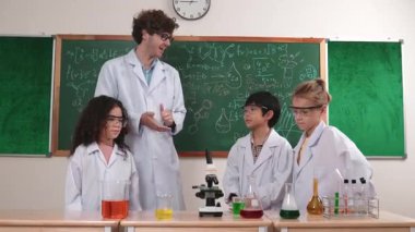 Zeki fen öğretmeni bilim teorisini çeşitli çocuklara öğretirken, mutlu ilkokul öğrencisi de mikroskop ve renkli çözeltilerle masada kimya sıvısını dinleyip öğreniyor. Pedagoji.