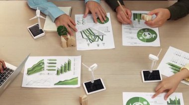 Eko evi projesini yel değirmeni tasarım modeli ve karbon ayak izini azaltmak için yeşil enerji kullanım grafiği ile toplantı masasında tartışan harika bir iş ekibi. Dünyayı kurtarın. Eline odaklan. Tanımlama.