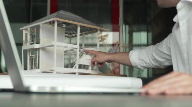 Kabiliyetli beyaz mimar el yapımı ev tasarımını dizüstü bilgisayardaki model ve plan ile karşılaştırın. Laptop analiz verilerini kullanan profesyonel proje yöneticisi. Eline odaklan. Yönlendirici.
