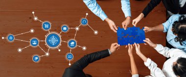 Profesyonellerden oluşan çeşitli bir ekip, modern iş bağlantıları ve takım çalışmalarını temsil eden dijital simgelerle çevrili stratejik planlamayı sembolize eden bir bulmaca üzerinde işbirliği yapıyor. Dostluk