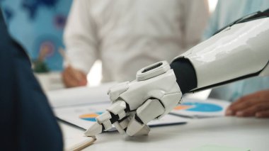 Gelecekçi bir robotik el, yenilikçi teknoloji ve takım üyeleriyle çizelgeler ve belgeler etrafında işbirliği sergileyen bir iş toplantısına aktif olarak katılır.