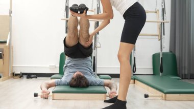 Pilates eğitmeni bir müşteriye paspasın üzerinde bacak esnetme sırasında rehberlik ediyor. İspanyol öğrenci, esnekliği ve çekirdek istikrarı artırmak için ters çatırtı ya da omuz duruşu yapıyor. Sağlık konsepti. Alışkanlık.