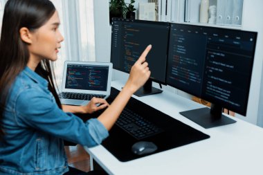 İnternet sitesinde kodlama programı uygulaması olan ve kot gömlek giyen bilgisayar hakkında bilgi veren IT geliştiricisi genç bir Asyalı kız. Güvenlik programlarıyla çevrili iki ekran. Taktik.