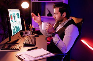 Gülümseyen zeki işadamı, elinde kahve fincanı olan satış ekibiyle buluşuyor ve geceleri Mor Neon Light Home Office 'deki bilgisayar ekranında ürün hedef pazarını araştırıyor. Tahmin et..