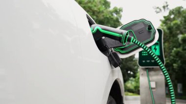 Doğal yeşil araba parkındaki ekolojik temiz enerji şarj istasyonundan gelen fütürist akıllı EV şarj aletinin şarj ettiği elektrikli araba. Alternatif enerji kullanan gelecekçi çevre dostu elektrikli araba. İnceleyin